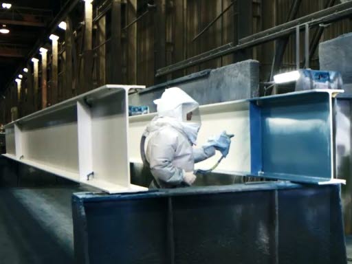 A technician applies paint to a primed steel girder at High Steel Structures